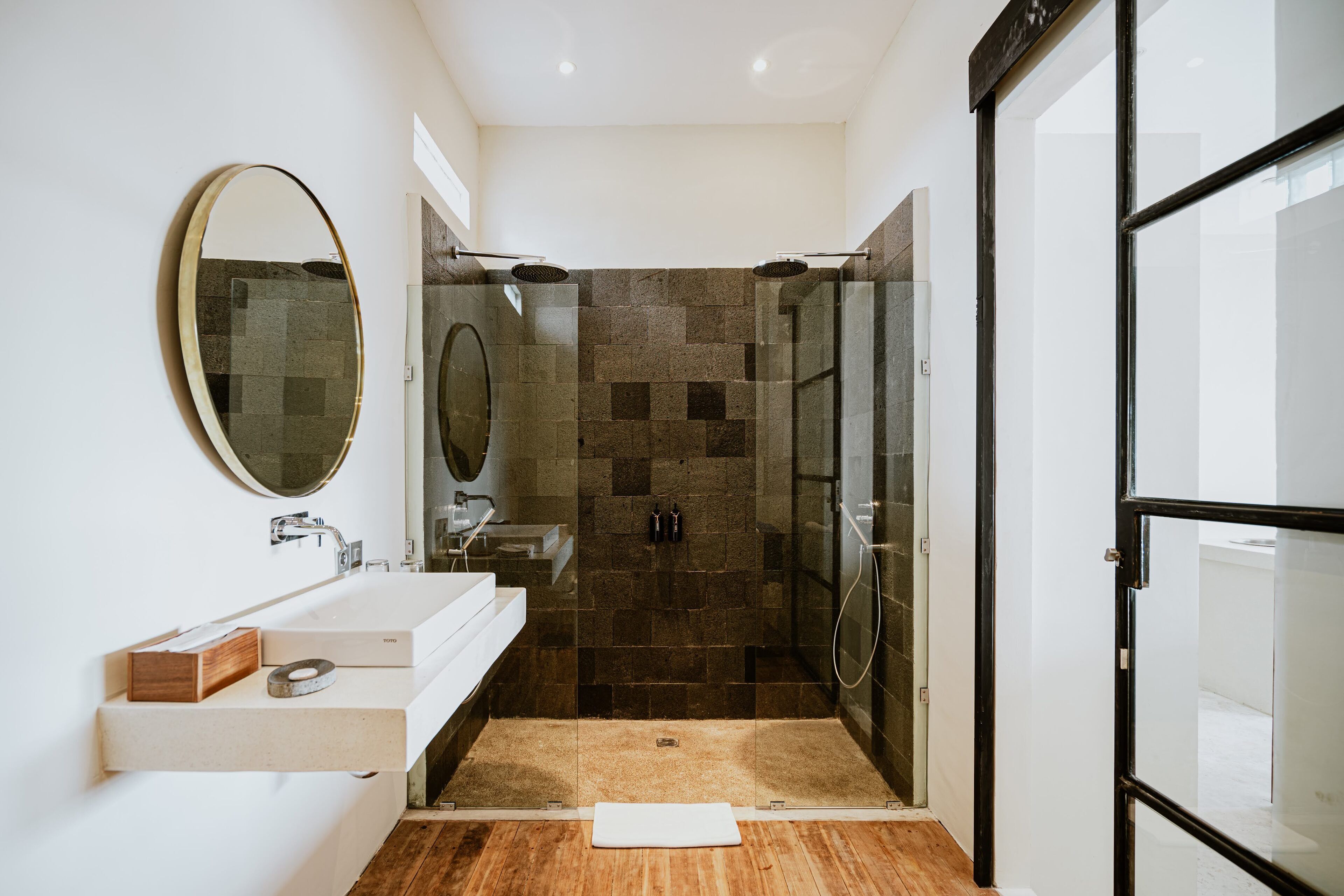 A modern bathroom with a glass shower enclosure, a wooden floor, and a white vanity with a mirror.