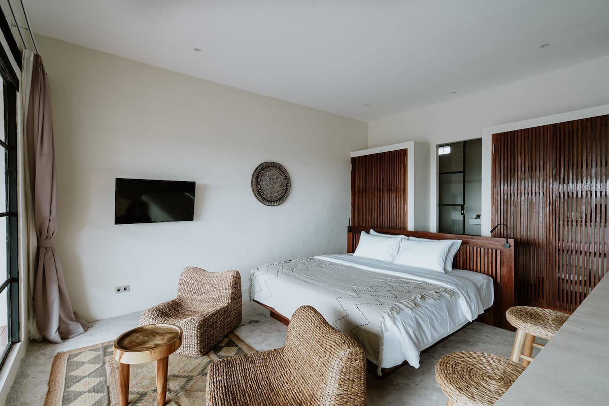 Une chambre à coucher avec un lit, deux fauteuils en osier, un téléviseur et une cloison en bois.
