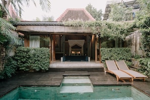 A poolside area with a wooden deck, two lounge chairs, and a small pool.
