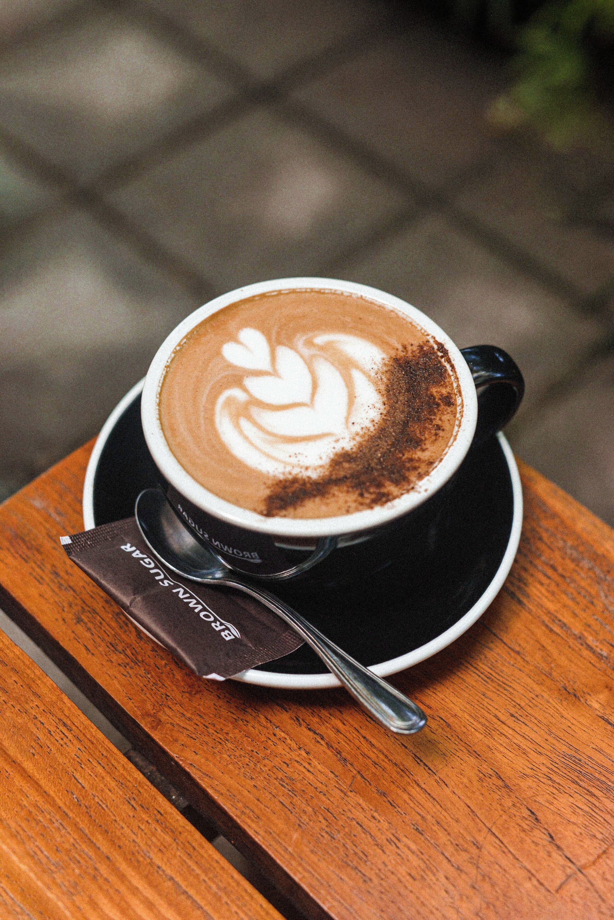 Eine Kaffeetasse mit Latte-Art auf einem Untertasse, platziert auf einem Holztisch.