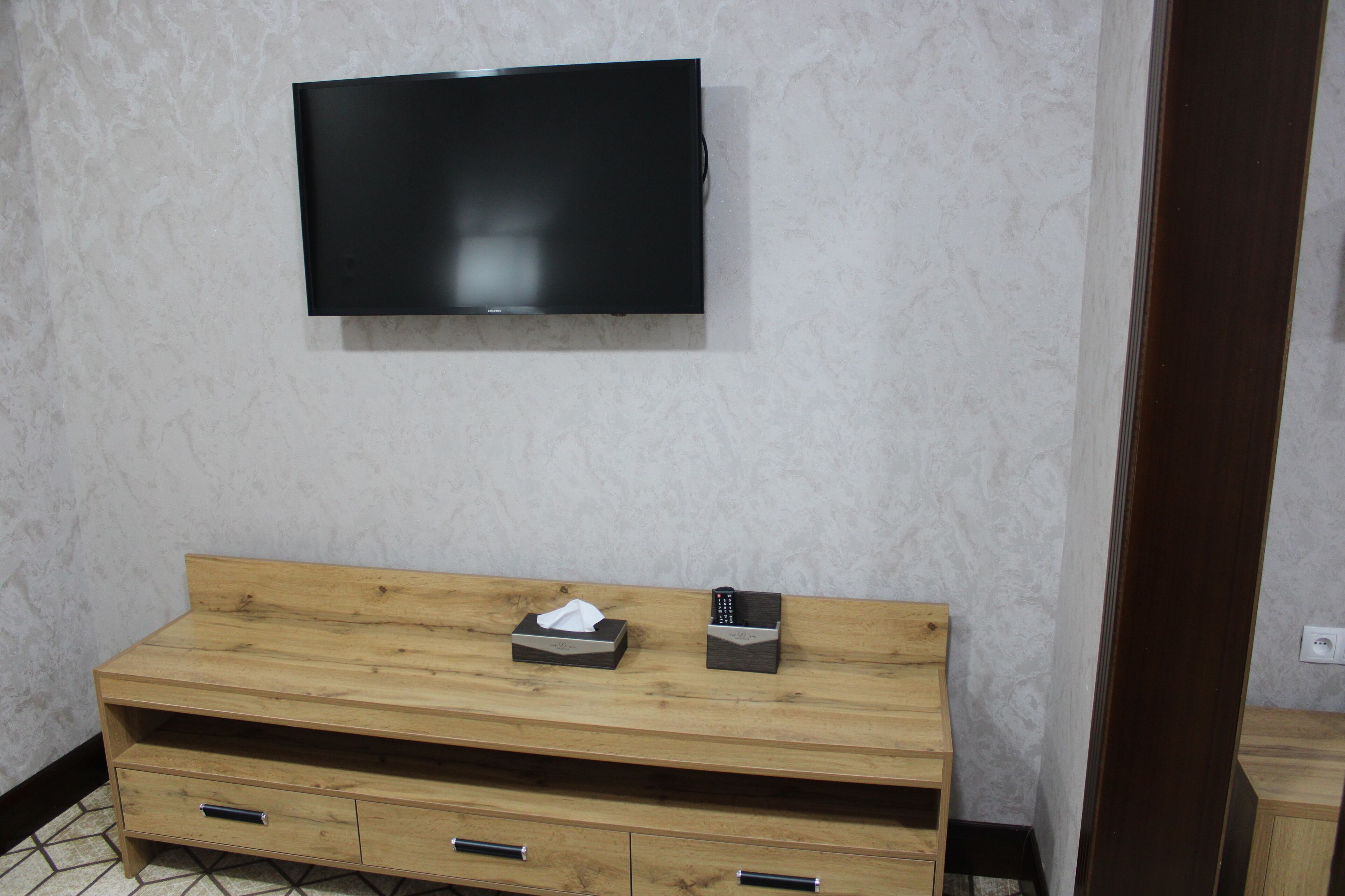 Une chambre avec une coiffeuse en bois, un téléviseur fixé au mur et une boîte à mouchoirs.