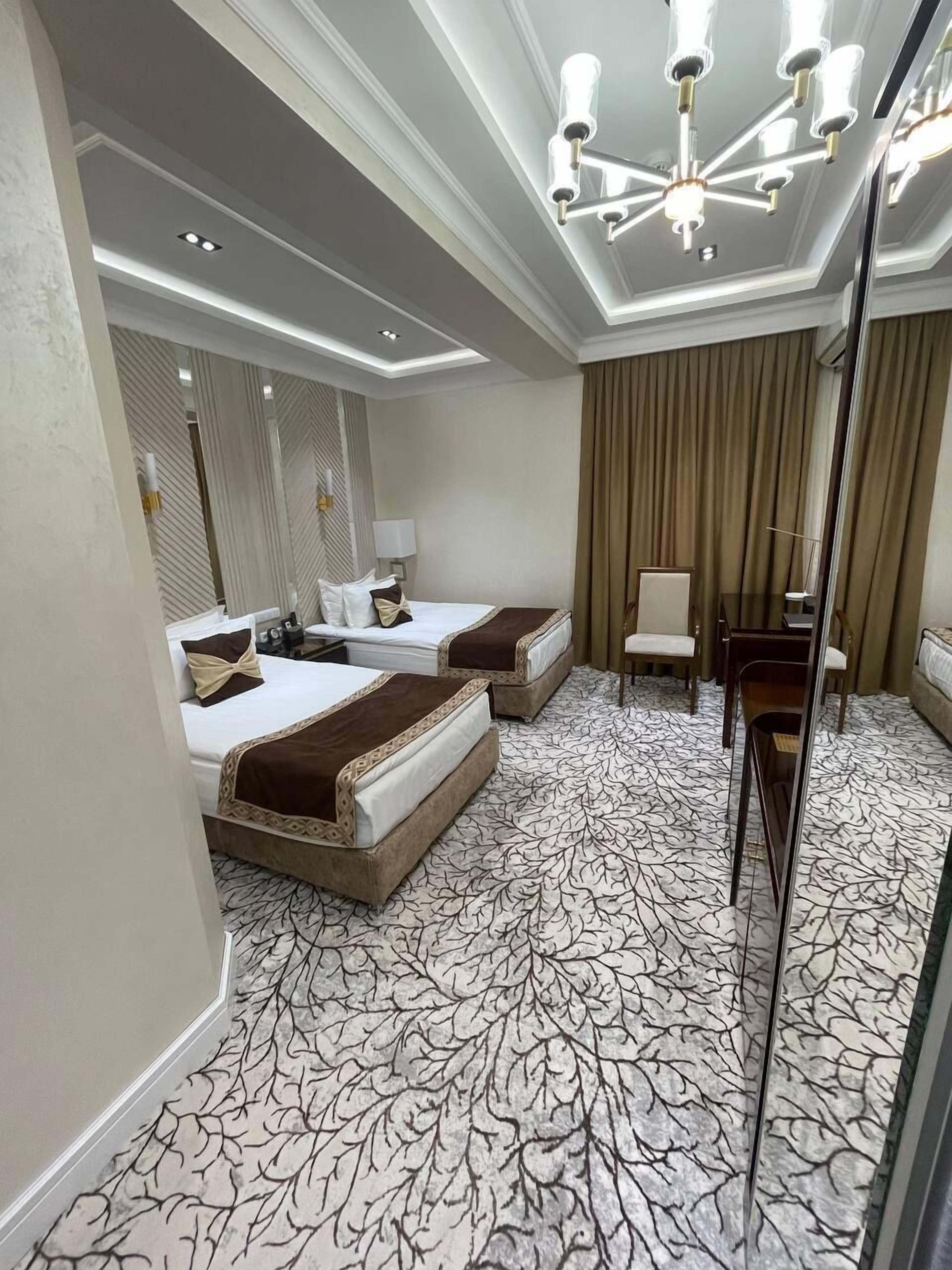 A hotel room with two beds, a large mirror, a chandelier, and a patterned carpet.