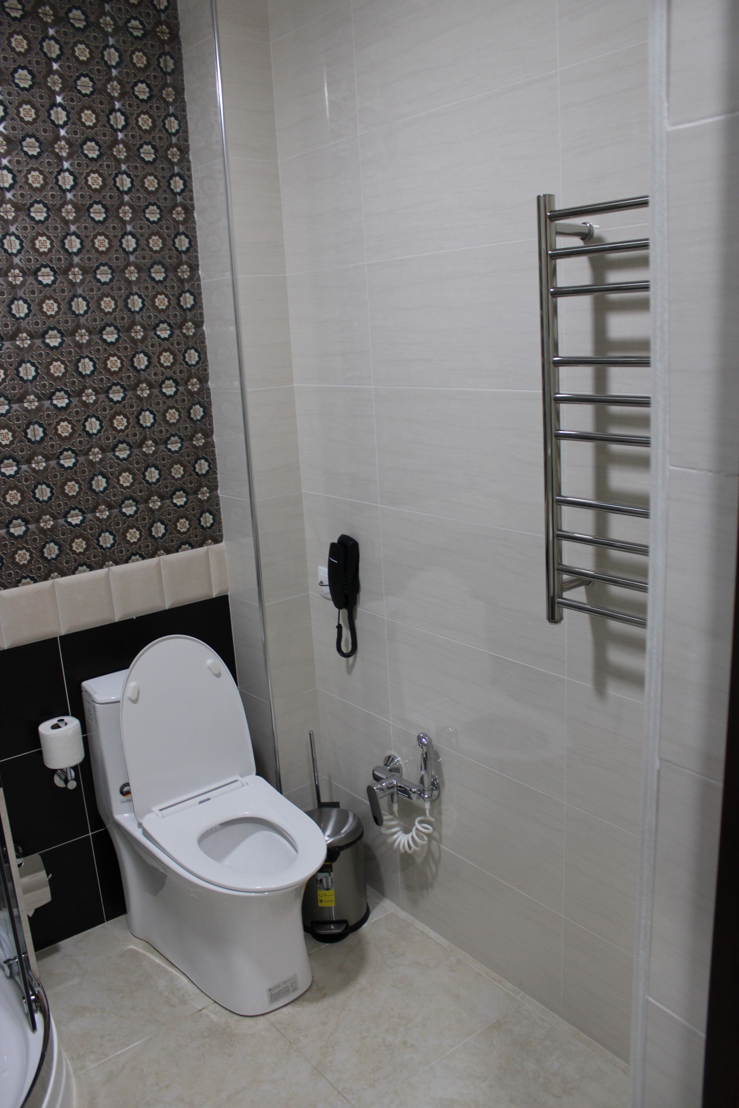 Une salle de bain équipée de toilettes, d’une poubelle, d’un sèche-mains et d’un porte-serviettes.