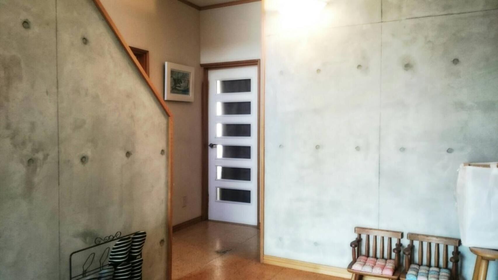 A hallway with a wooden staircase, a door with frosted glass panels, and a bench with striped cushions.