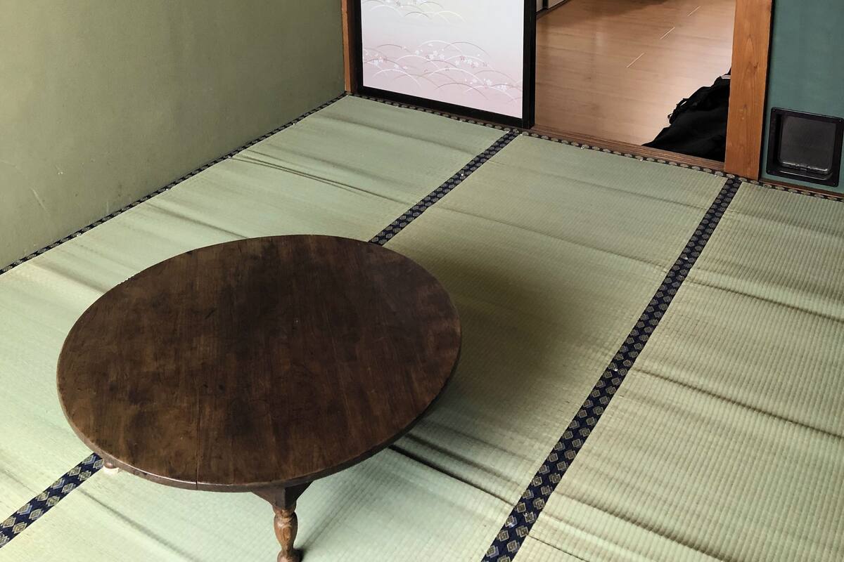 A tatami mat room with a wooden table, a sliding door leading to another room, and a small table with a chair.