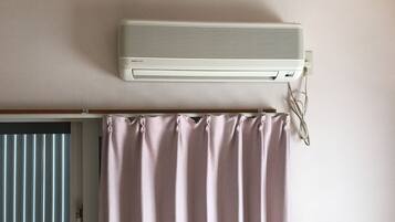 Una habitación con un aire acondicionado blanco montado en la pared, una puerta con persiana vertical y una cortina rosa.