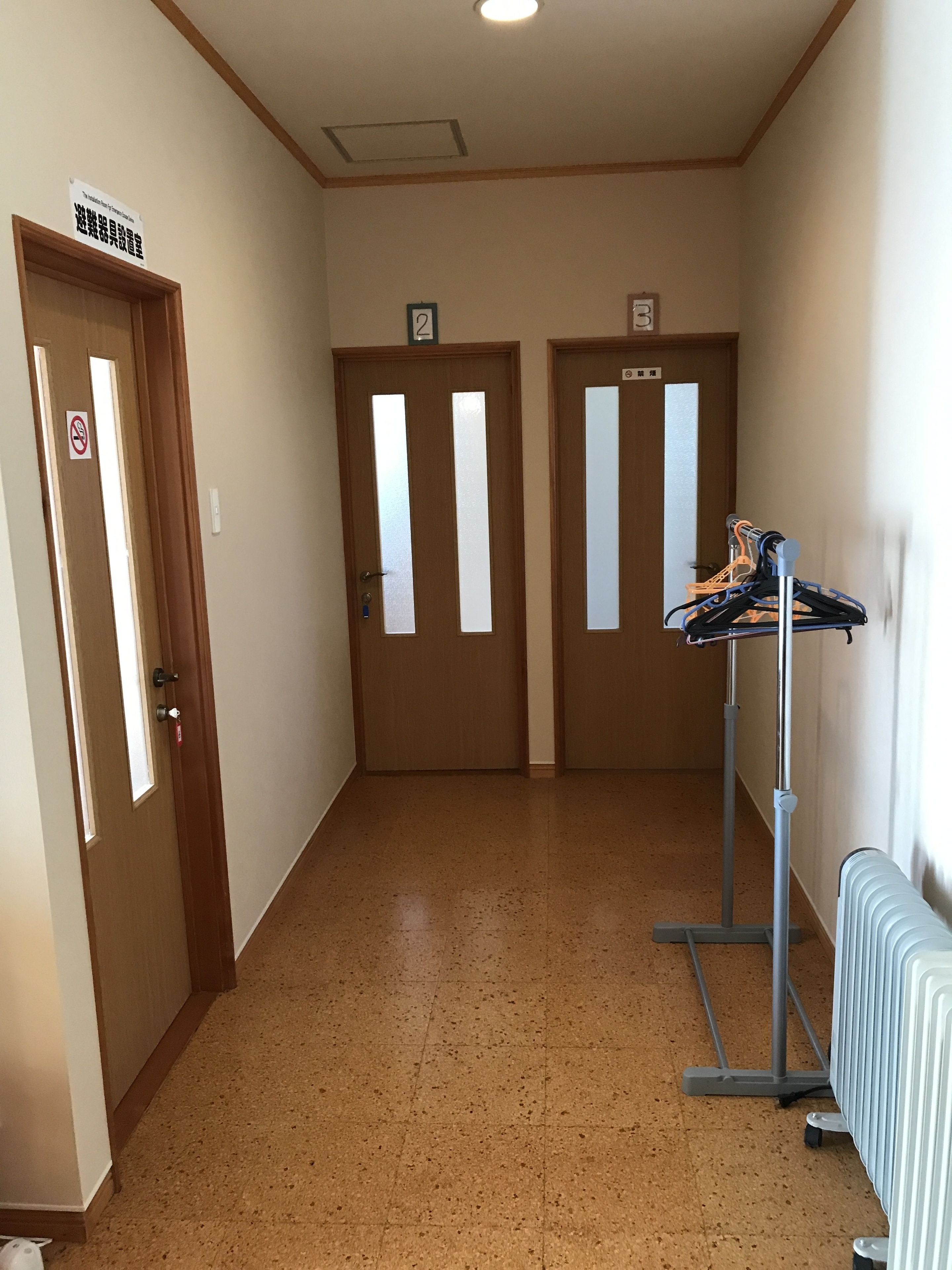 Ein Korridor mit zwei Türen, jede mit einer Nummer und einem Rauchverbot-Schild gekennzeichnet. Auf der rechten Seite ist ein Kleiderständer mit Kleiderbügeln zu sehen.