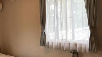 Quarto com cama, radiador, janela com cortinas e luminária fixada na parede.
