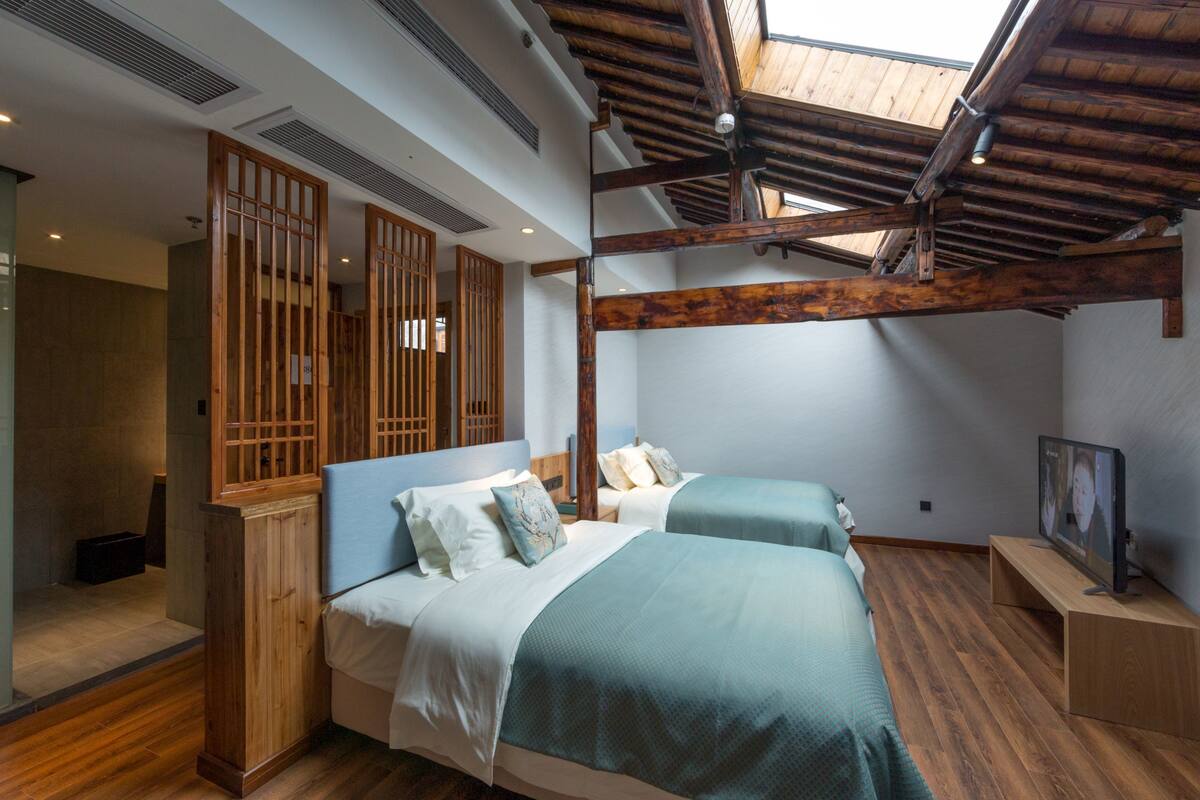 Une chambre avec deux lits, des poutres en bois, une lucarne et un téléviseur posé sur un meuble en bois.
