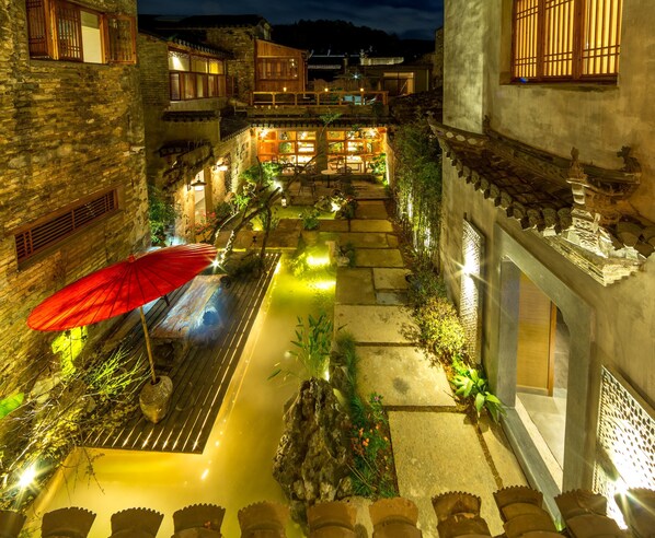 A courtyard with stone pathways, a red umbrella, and traditional wooden buildings with illuminated windows. - Huangshan Huanchun·Bingyu Resort (Huangshan)