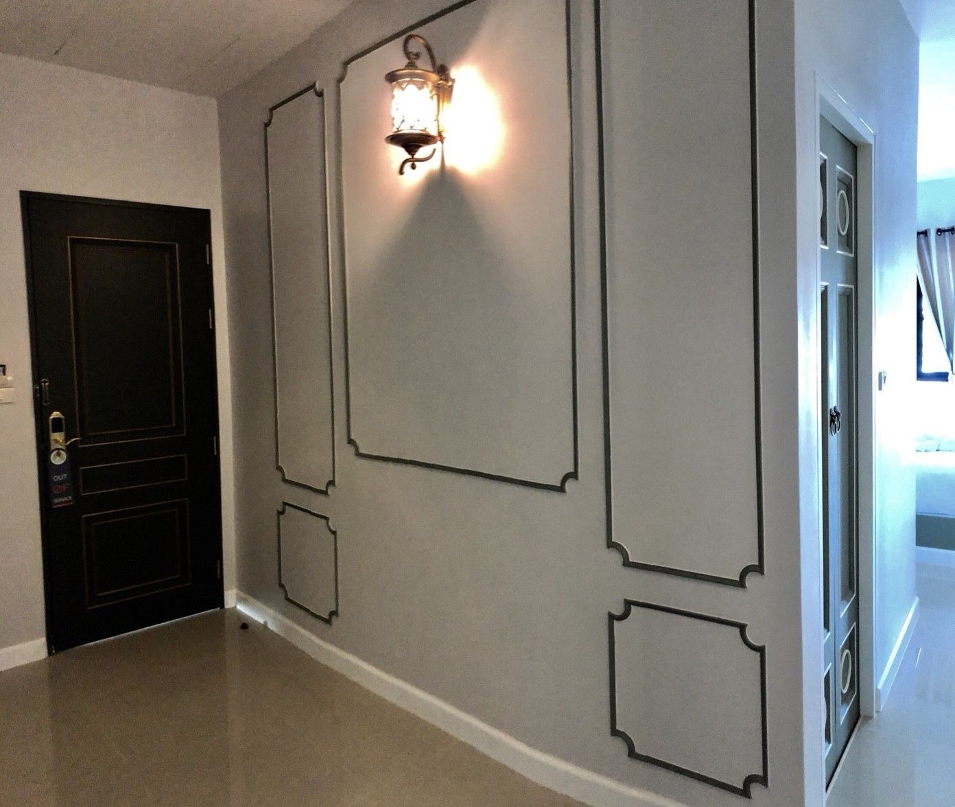 A hallway with a black door, a wall-mounted light fixture, and a door with a lock.
