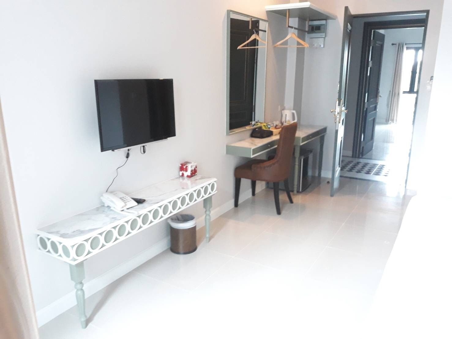 A modern hotel room with a flat-screen TV mounted on the wall, a small desk with a chair, and a mirror above the desk.