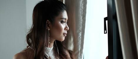 A person standing by a window with curtains, wearing a white lace dress.