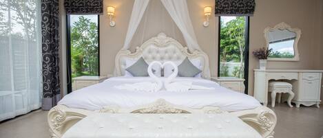 Una cama grande con cabecera y piecera ornamentados, dos mesitas de noche, un tocador y una ventana con cortinas.