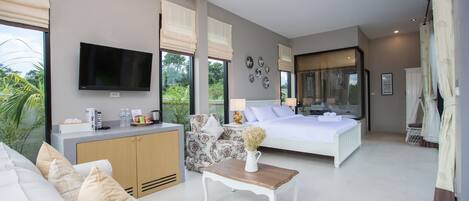 Quarto moderno com uma cama grande, televisão, escrivaninha e vista para o exterior.