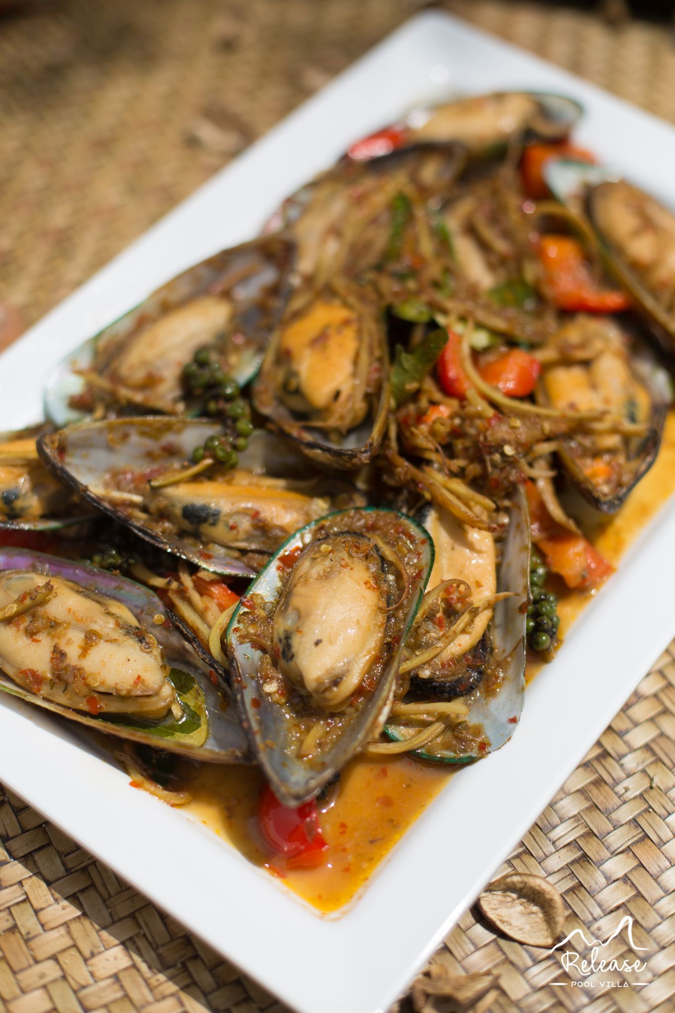 A dish of mussels with vegetables and sauce on a white plate.