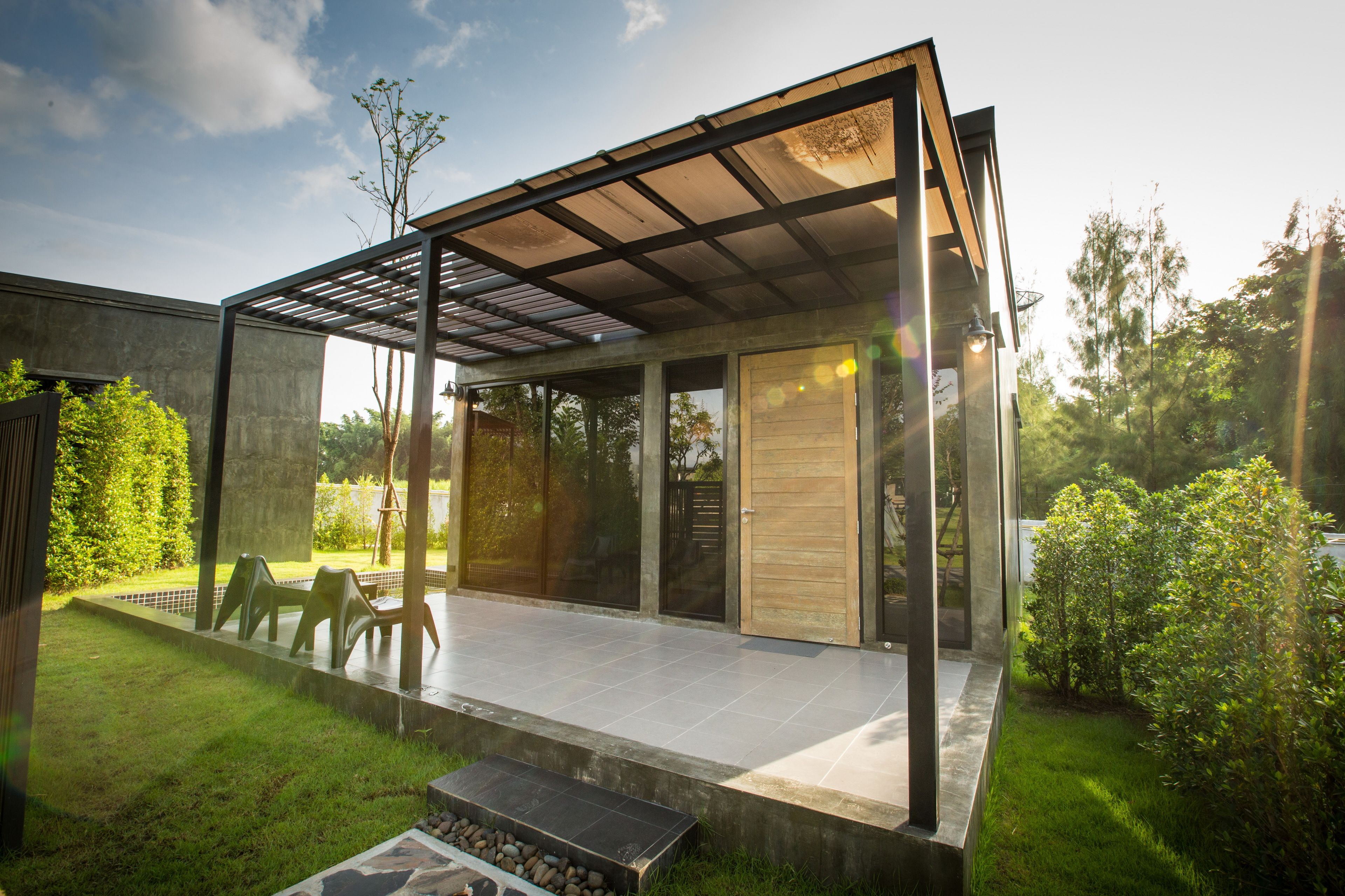 A modern outdoor patio with a glass enclosure, a seating area, and a well-maintained garden.