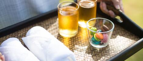 Uma bandeja com duas chávenas de chá, um prato de macarons e duas toalhas enroladas sobre um tapete tecido.