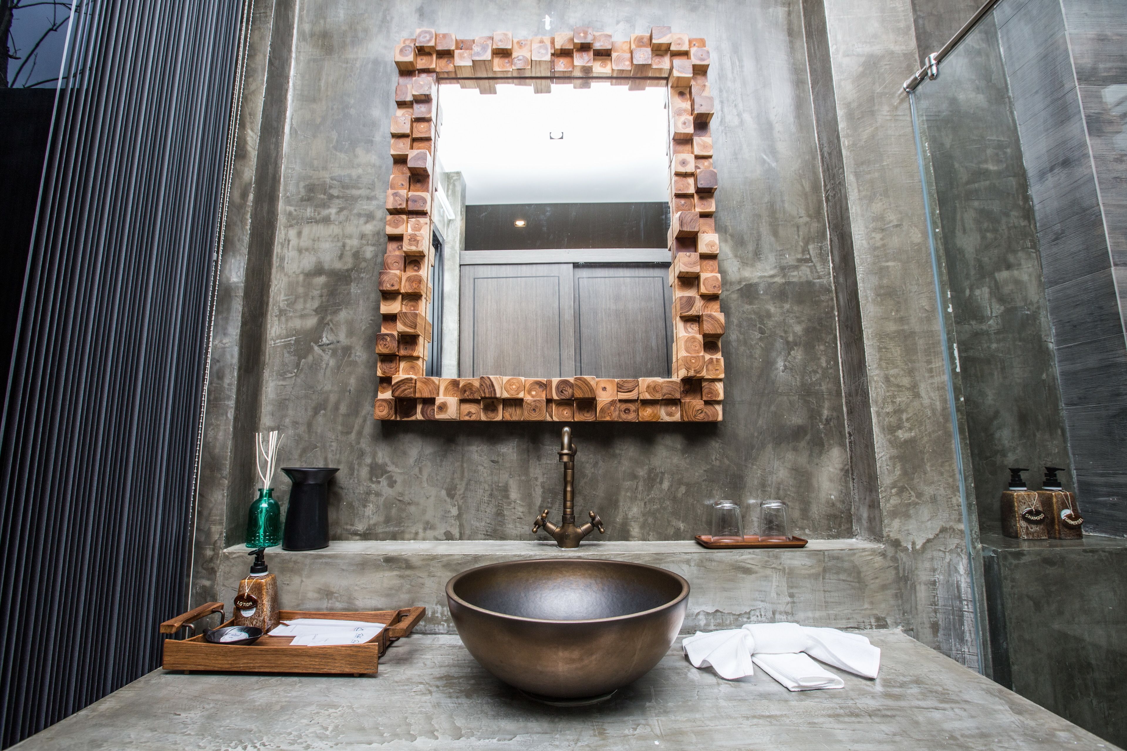 A bathroom with a large wooden-framed mirror, a central sink with a faucet, and a wooden tray with toiletries.