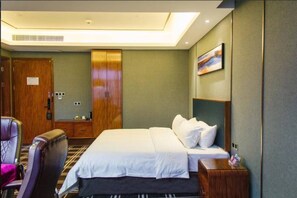 Habitación de hotel con una cama, una silla, un armario de madera y un cuadro en la pared.
