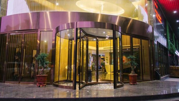 En modern hotellentrél med en roterande dörr, glaspartier och krukväxter.