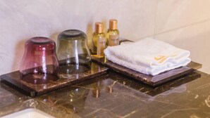En badrumsmöbel med en bänkskiva i marmor, en rosa tvåldispenser, en genomskinlig tvålpump i glas, två flaskor lotion och en vikt hopfälld vit handduk med en logotyp.