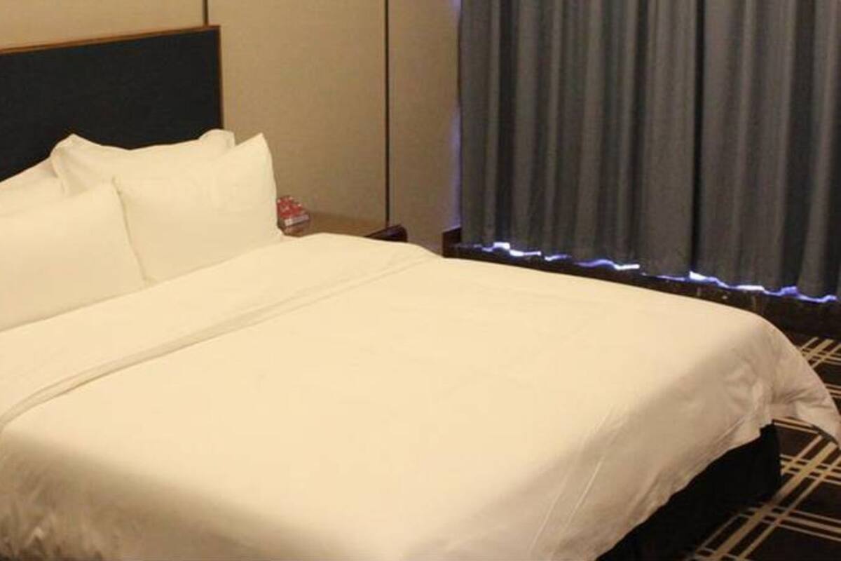 Un lit bien fait, avec du linge de lit blanc, dans une chambre d’hôtel.