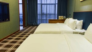 Ett hotellrum med två sängar, ett stort fönster med gardiner, en tv på väggen till vänster och en tavla ovanför sängen.