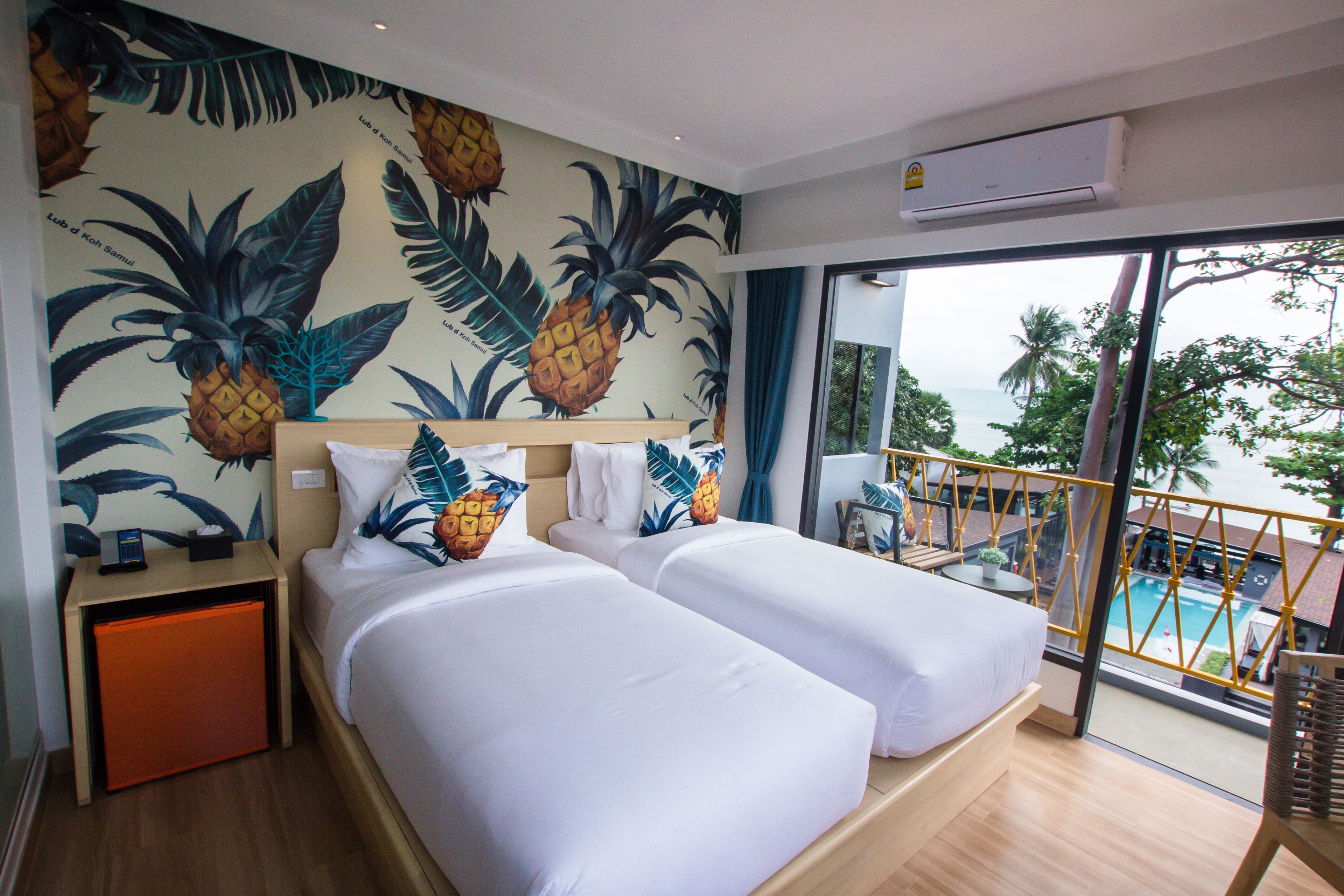 A hotel room with two beds, a large window with a view of a pool and palm trees, and a tropical-themed wall mural.