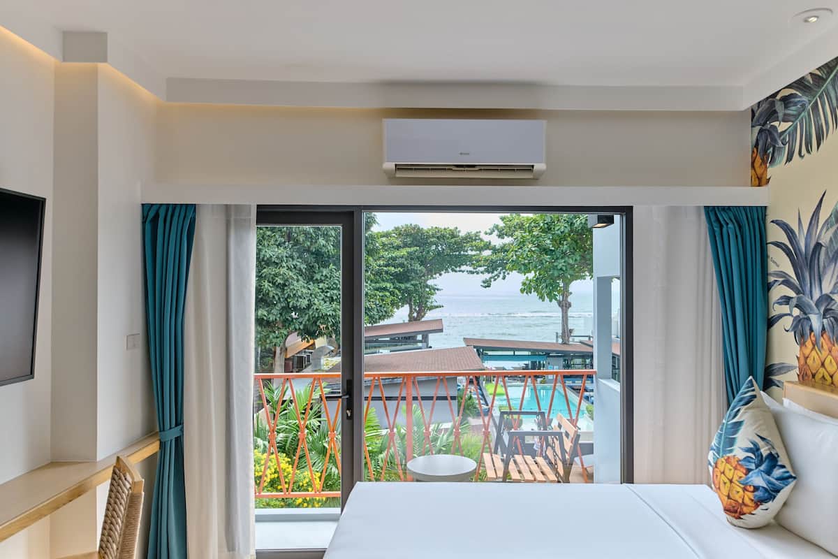 Une chambre d’hôtel dotée d’une grande porte-fenêtre coulissante donnant sur un balcon avec une piscine et un espace salon extérieur.