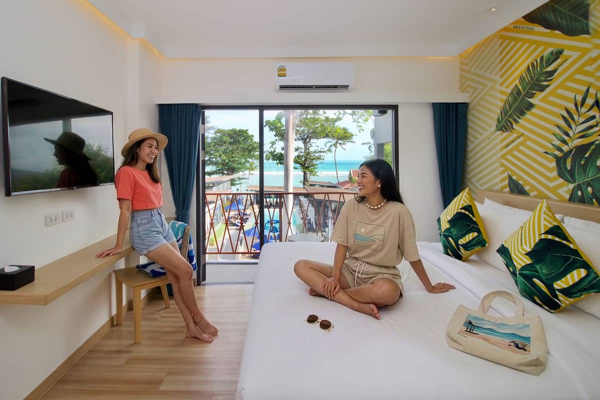 Une chambre d’hôtel avec un lit, une télévision, un balcon donnant sur la piscine et un mur décoré sur le thème tropical.