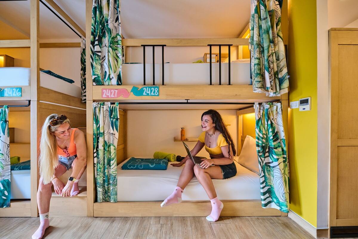 Une chambre avec un lit superposé, un plafond en bois, un petit bureau et un mur jaune.