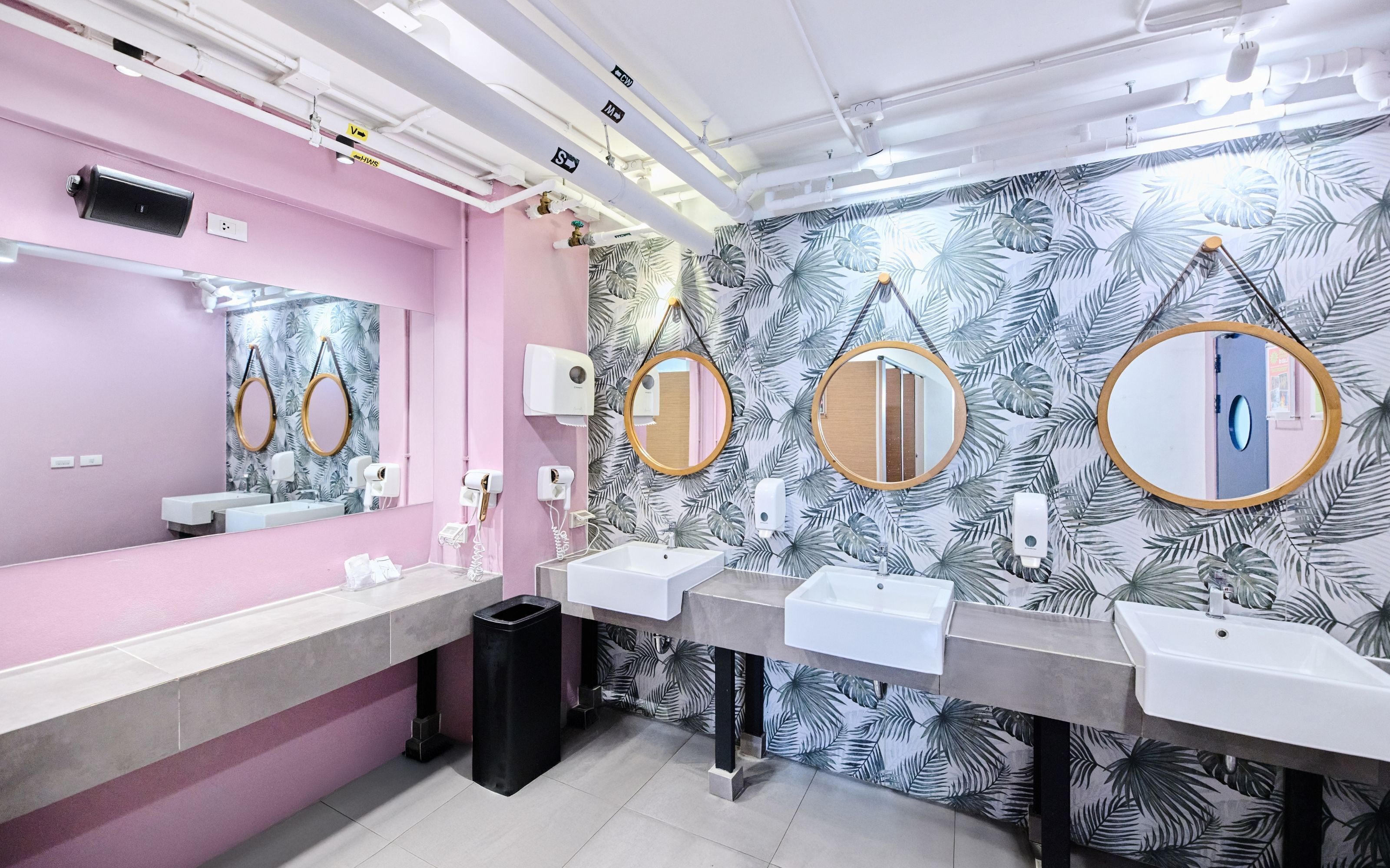 A modern bathroom with pink walls, three sinks, and mirrors with wooden frames.