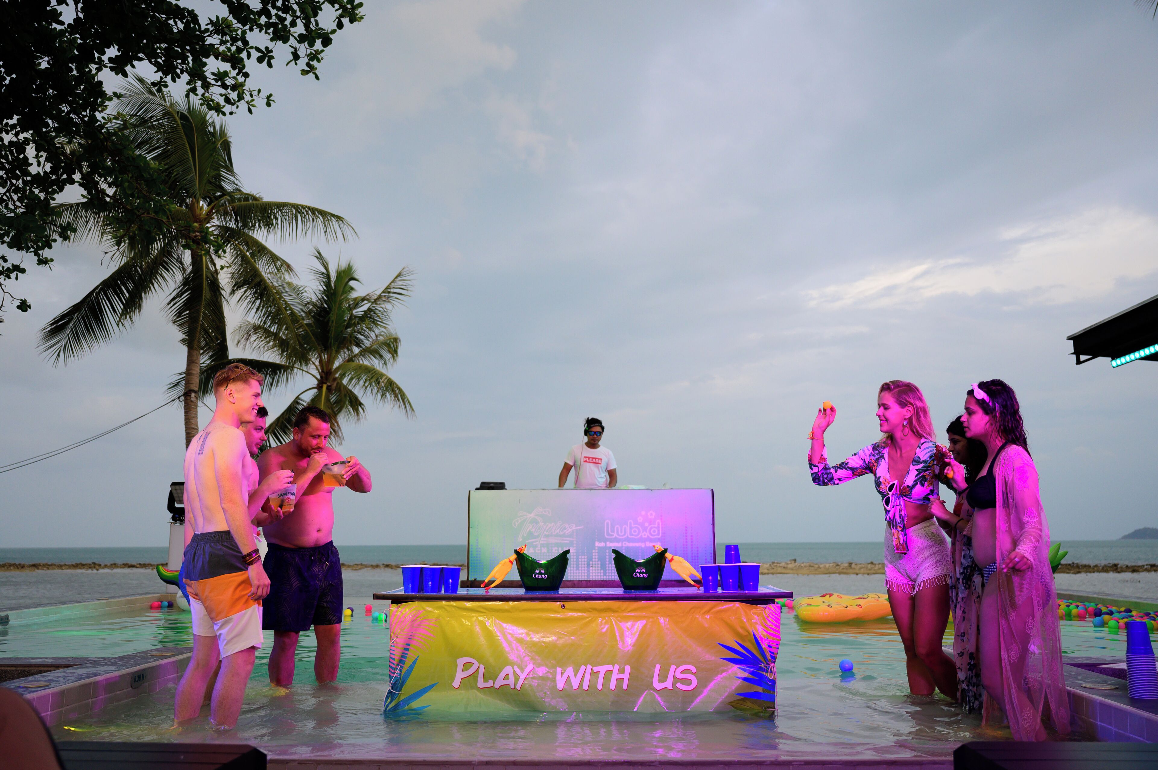 A poolside event with a DJ booth and people socializing.
