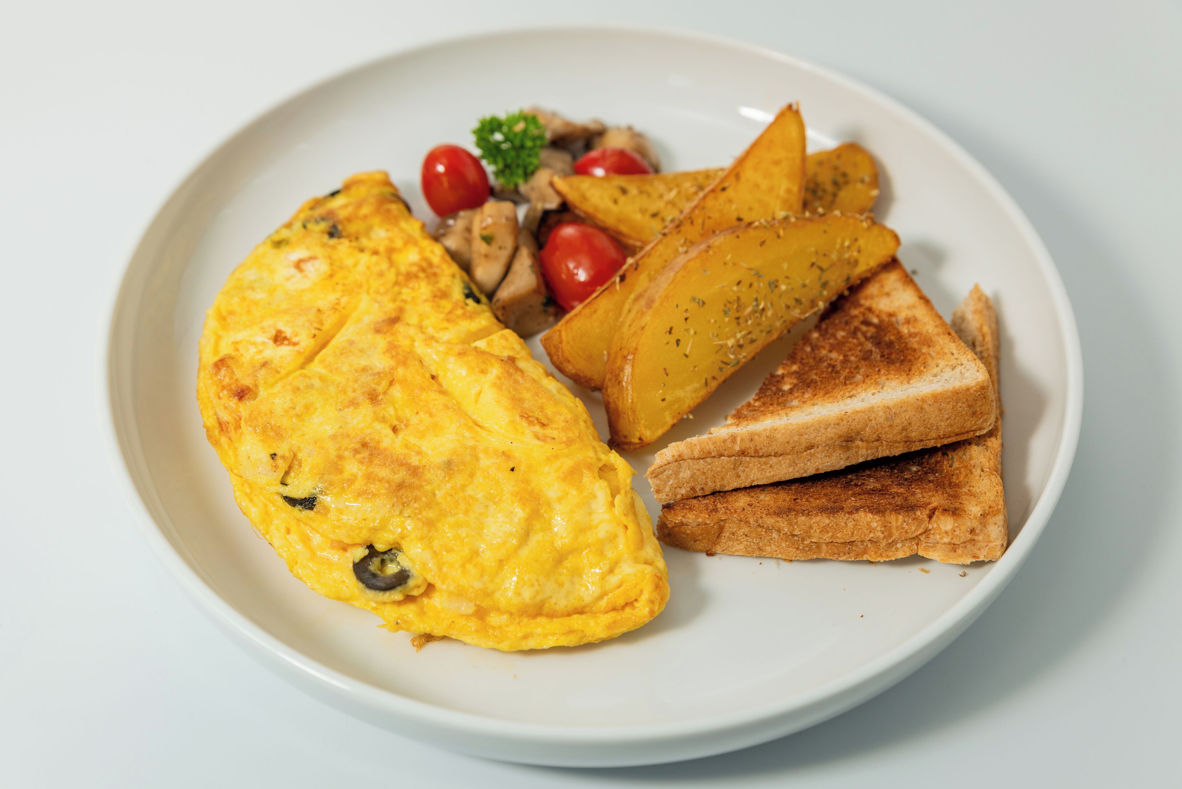 A plate with an omelette, toasted bread, roasted potatoes, and cherry tomatoes.