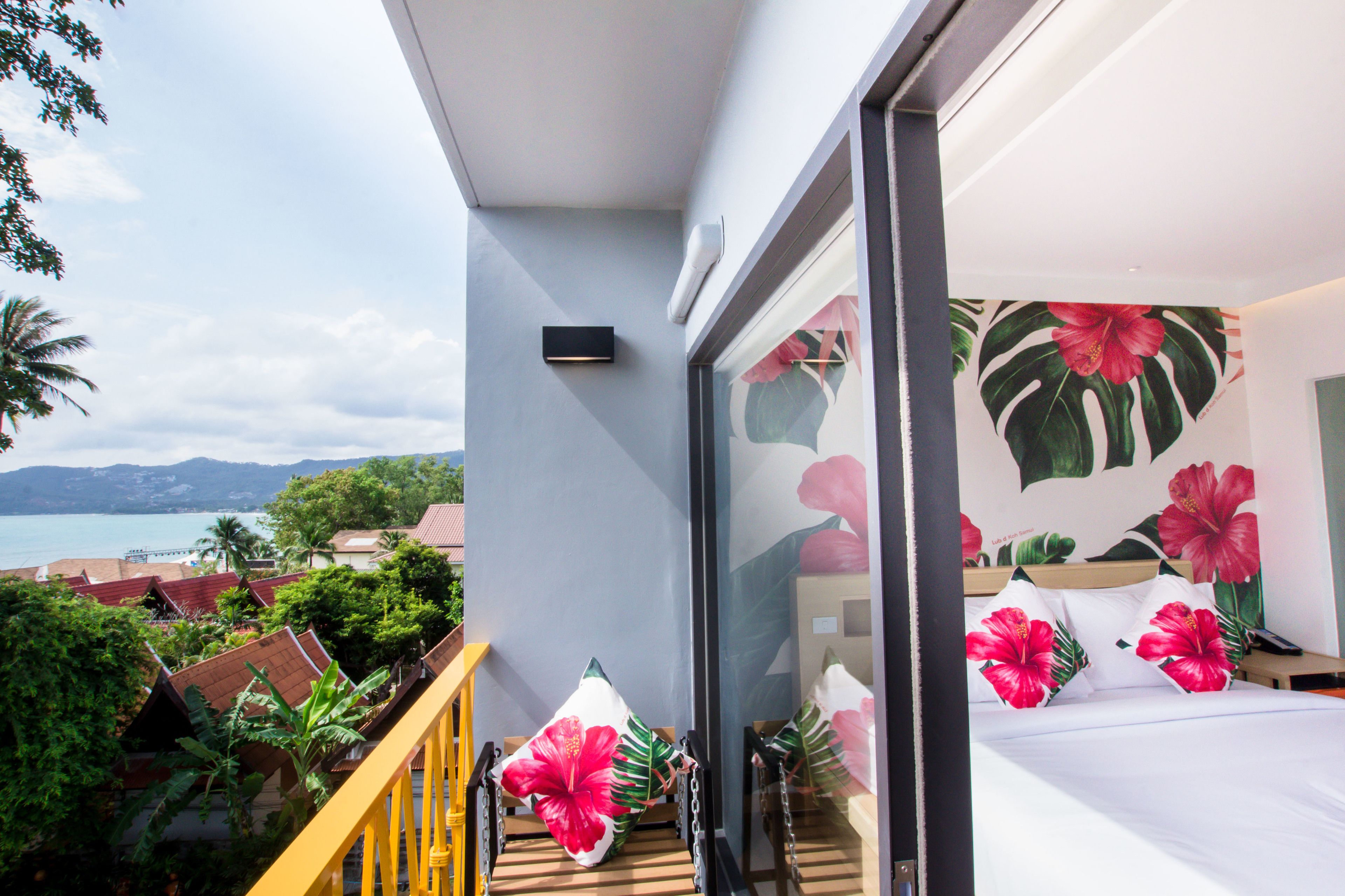 A balcony with a view of the sea and mountains, a bed with floral pillows, and a modern interior design.