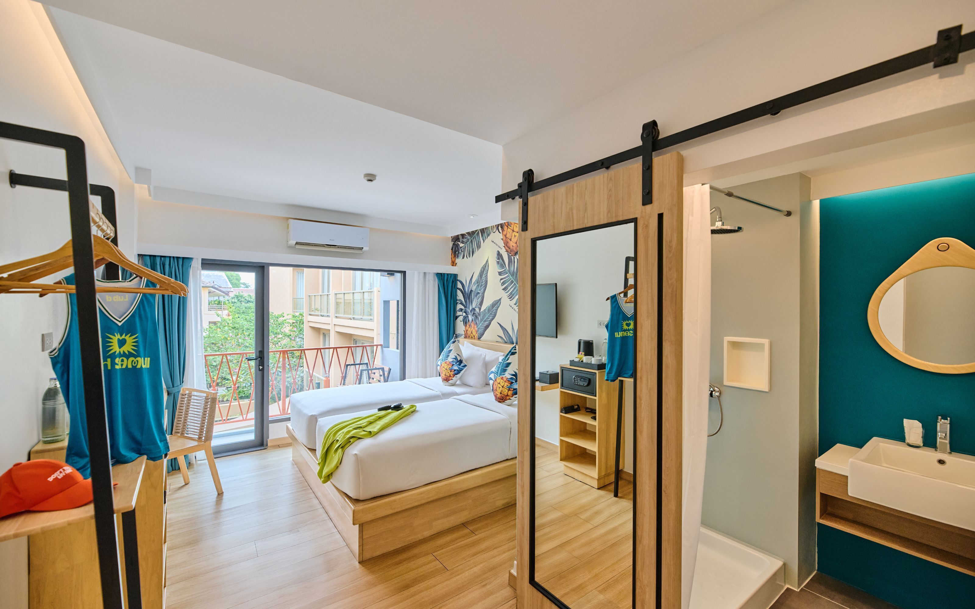 A modern hotel room with a bed, a bathroom, a balcony, and a view of the city.