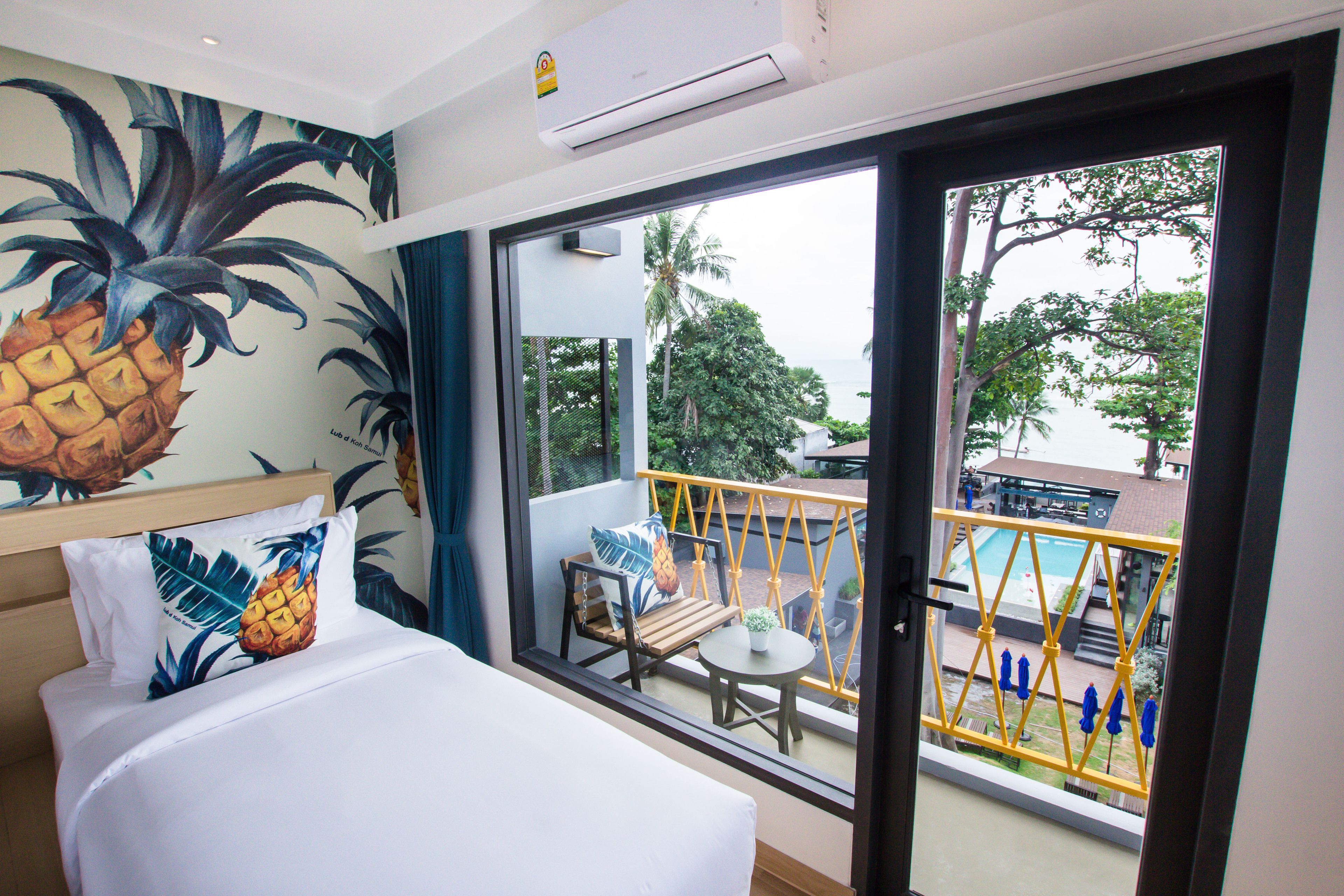 Habitación de hotel con cama, ventana con vista a una piscina y follaje, y un mural tropical en la pared.