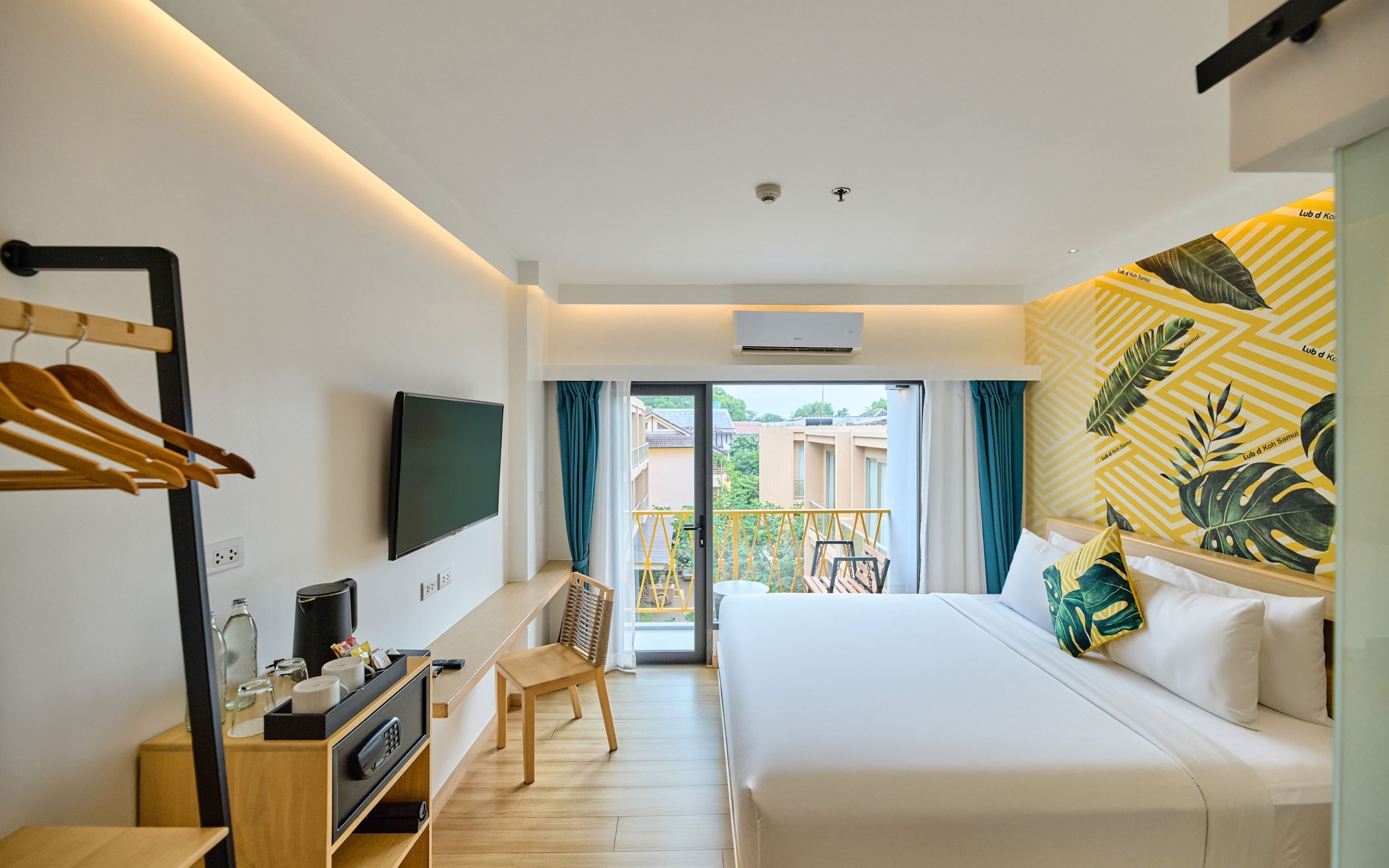 Une chambre d’hôtel équipée d’un lit, d’un bureau, d’une chaise, d’un téléviseur fixé au mur et d’un balcon donnant sur l’extérieur.