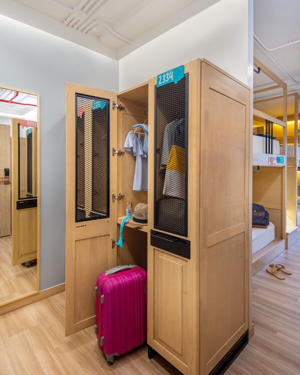 Habitación de hotel con un armario de madera, una maleta rosa y una cama nido al fondo.