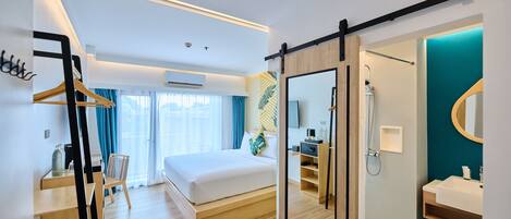 A modern hotel room with a large bed, a walk-in closet, a bathroom with a shower, and a view of the outdoors.