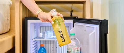 A person holding a bottle labeled "Lemonade" in front of an open refrigerator with shelves containing various beverages and a water dispenser.