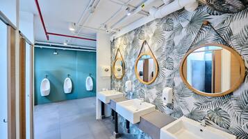 Un baño moderno con tres orinales, una fila de lavamanos y un revestimiento de pared con motivos de hojas tropicales.