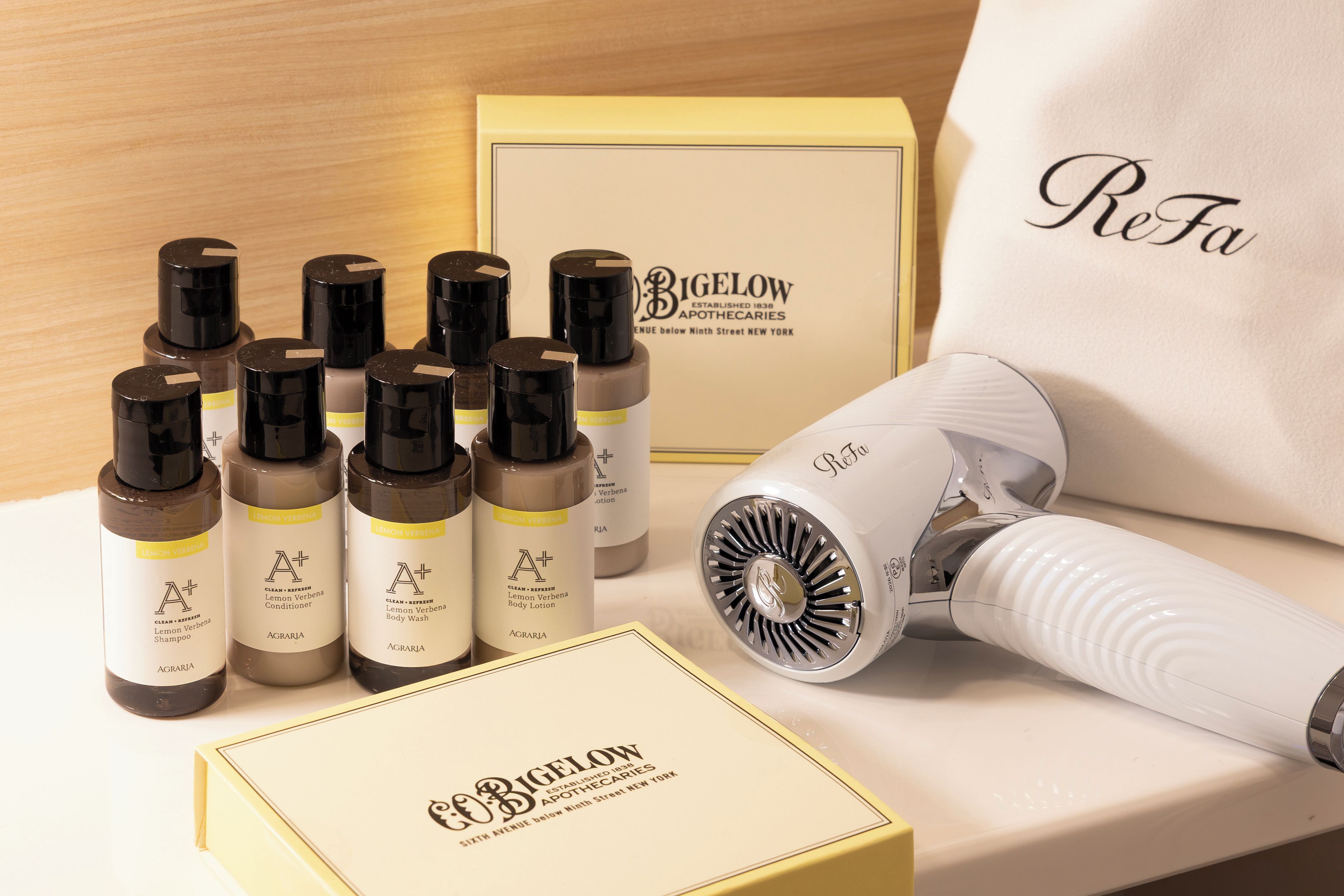 Una selección de productos de cuidado personal, incluyendo champús, acondicionadores, loción corporal y jabón de baño, junto con un secador de pelo y una caja con el logo de la marca.