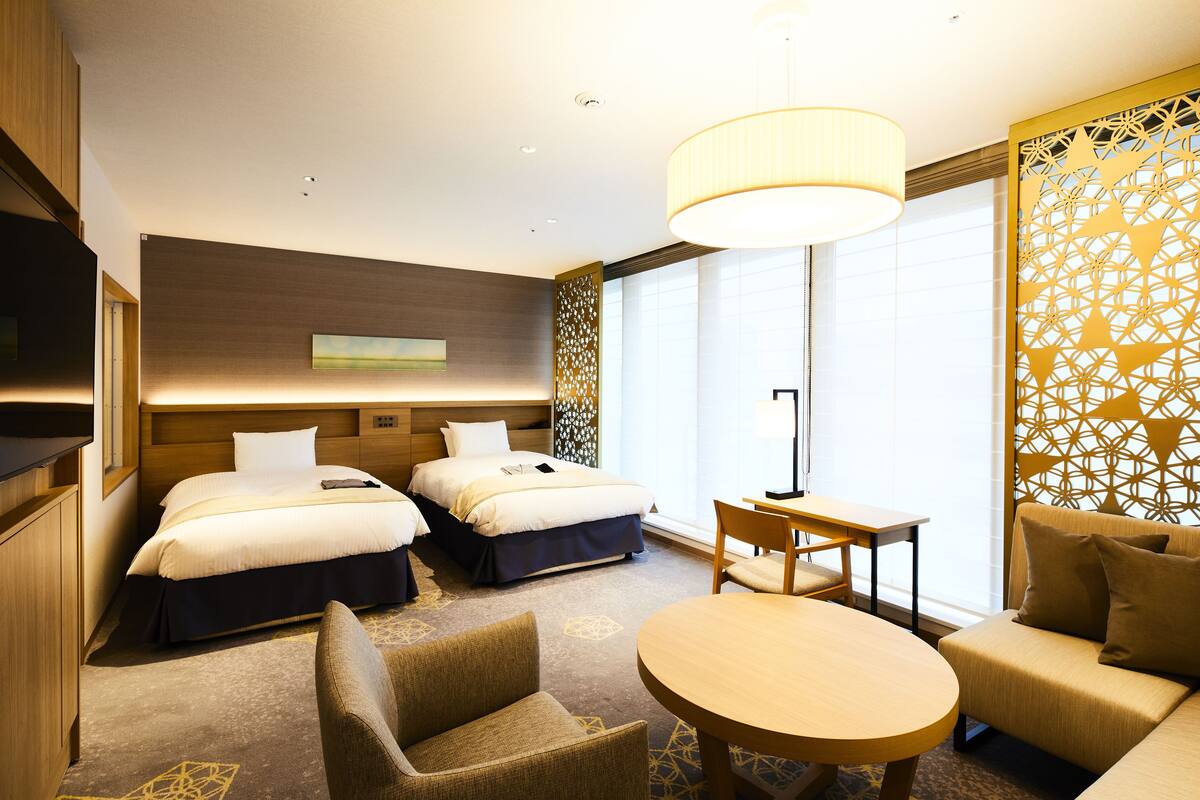 Habitación de hotel con dos camas, un sofá, una mesa redonda y un televisor.