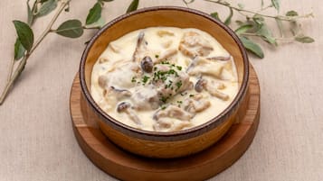 A bowl of creamy mushroom soup garnished with herbs, placed on a wooden coaster.