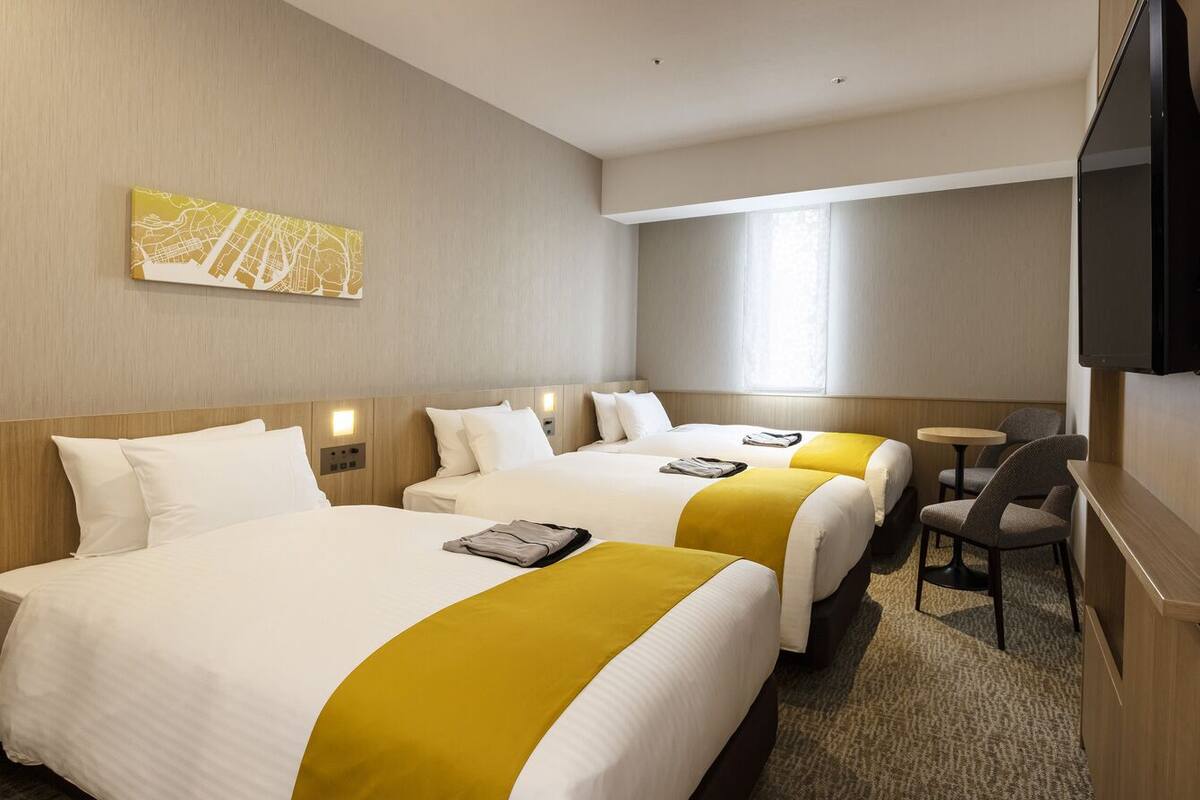 Una habitación de hotel con dos camas, televisión, una mesita y una silla.