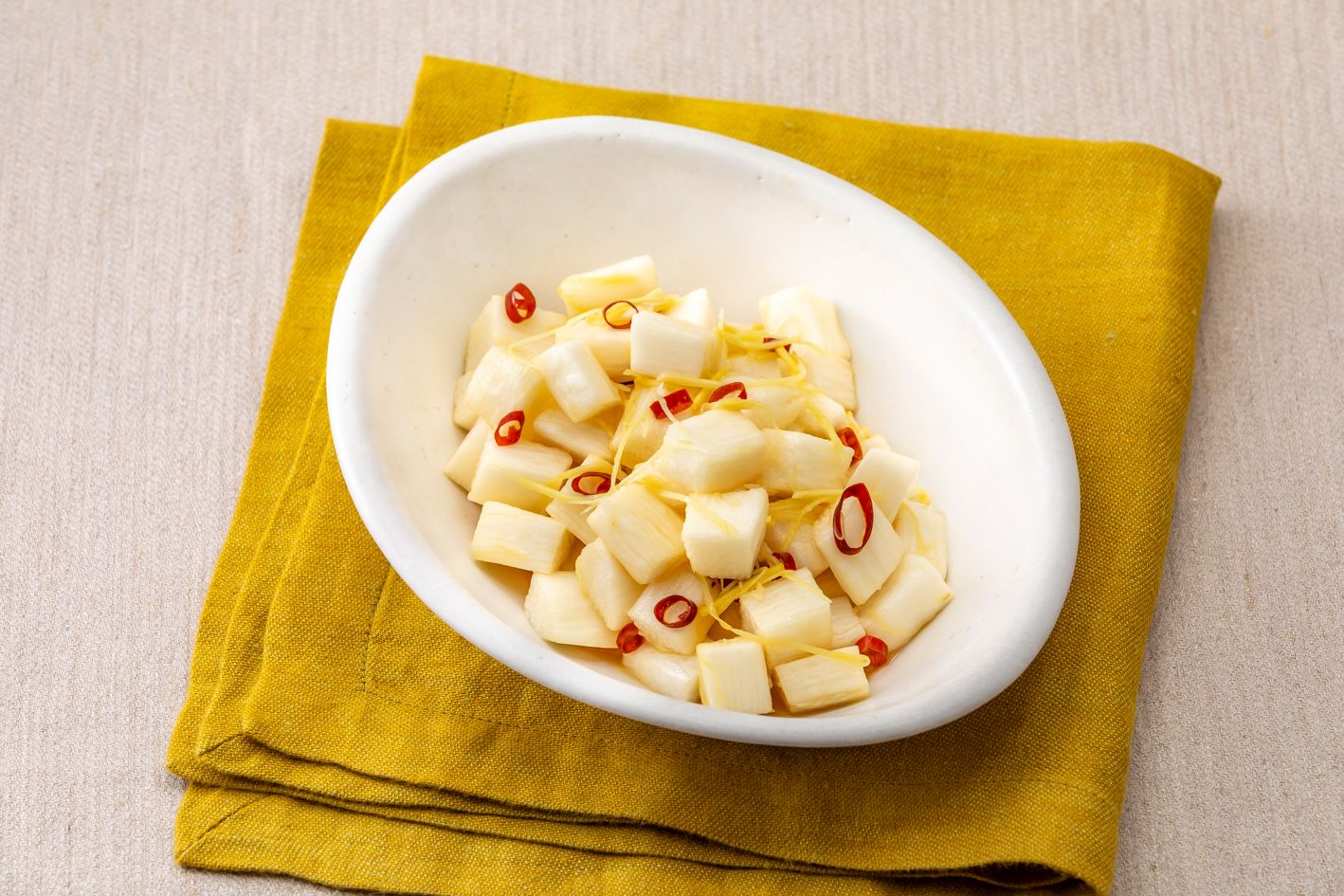 A white bowl filled with diced white food, possibly cheese, on a yellow cloth.