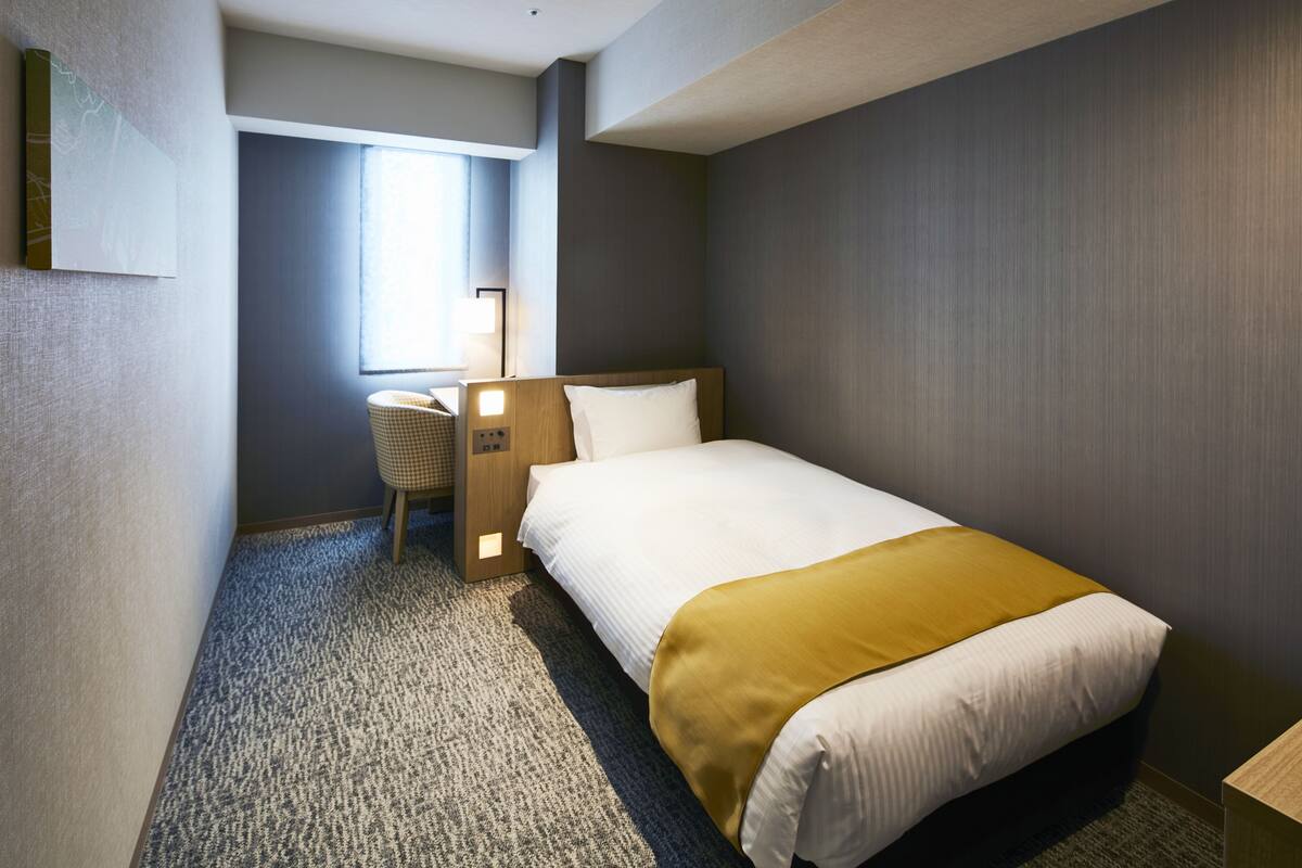 Una habitación de hotel con cama, escritorio, silla y ventana.