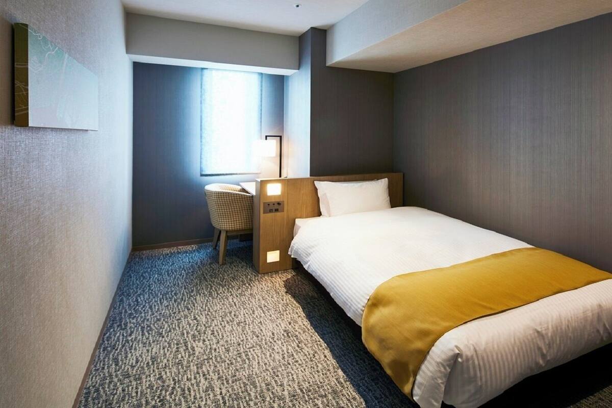 Una habitación de hotel con cama, escritorio, silla y ventana.